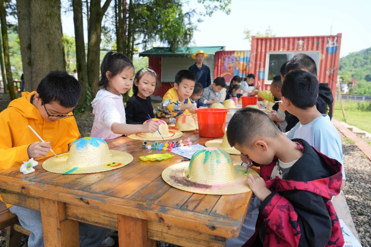 5月5日，北碚區天府鎮三間田藝術農場，參加研學活動的孩子們在樹林下給草帽繪畫。特約攝影 秦廷富
