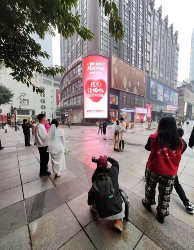 新人們在渝中區民政局解放碑CBD婚姻登記中心LED大屏前打卡留念。渝中區民政局供圖