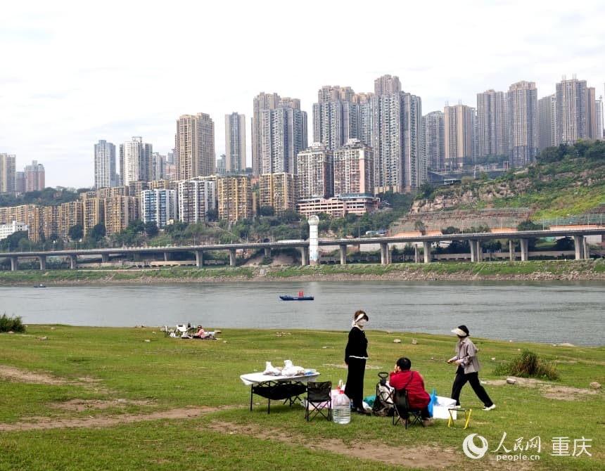 江滩上大片浅草铺成了天然的 “城市草原”，市民伴着江风与暖阳野餐闲谈。人民网 陈琦摄