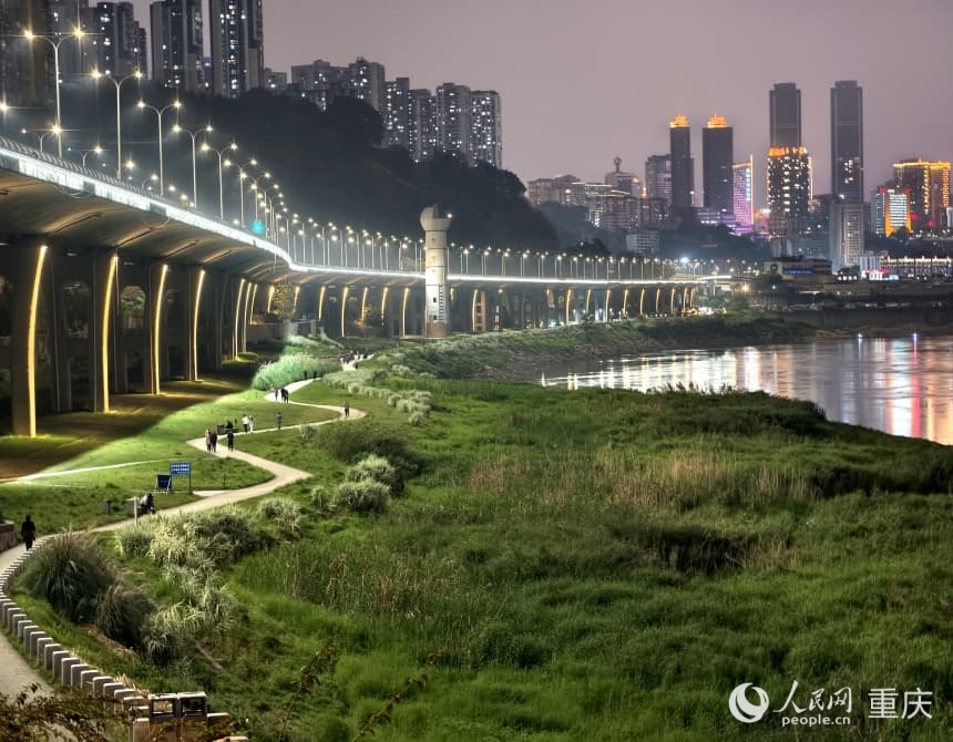 夜幕降临，重庆九滨路黄沙溪段蜿蜒的滨江步道上，市民伴着江风散步闲谈。人民网 陈琦摄
